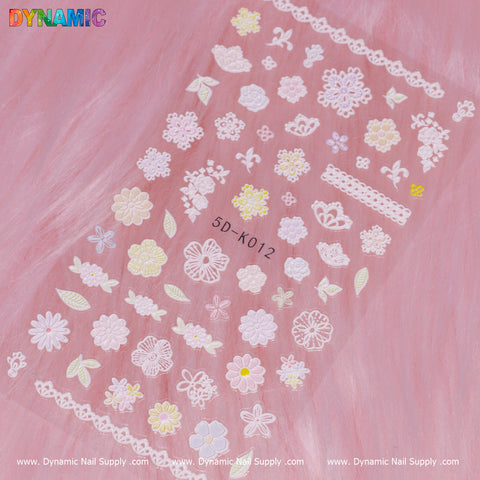 A sheet of the Floral Sticker (5D-K012) from Dynamic Nail Supply rests elegantly on a pink fur background. It showcases an intricate design of white and pastel-colored flowers, leaves, and lace patterns, topped with the word DYNAMIC in bold letters. The name Dynamic Nail Supply is repeatedly printed at the bottom.