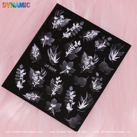 The Black and White Plant Sticker (JP3009) from Dynamic Nail Supply features intricate white floral and leaf designs, such as ferns and sprigs, on a soft pink background. "DYNAMIC" is displayed in colorful letters at the top left, accompanied by a logo with the URL at the bottom.