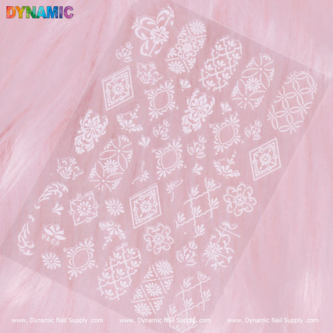 The Pattern Nail Sticker (R349) - White, showcasing an array of floral and geometric designs, is elegantly presented on a soft pink furry background. The Dynamic Nail Supply logo is prominently displayed at the top left in vibrant letters.
