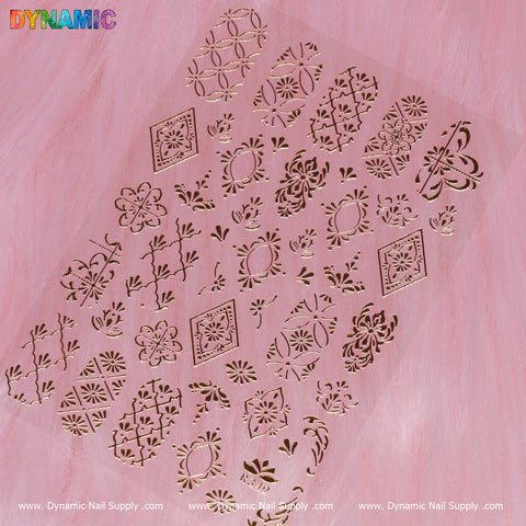A sheet of the Pattern Nail Sticker (R349) - Gold from Dynamic Nail Supply is displayed on a pink surface. Boasting intricate designs such as floral patterns, geometric shapes, and ornate motifs, these eye-catching stickers demand attention. The word "DYNAMIC" is prominently showcased in colorful, bold lettering in the top-left corner.