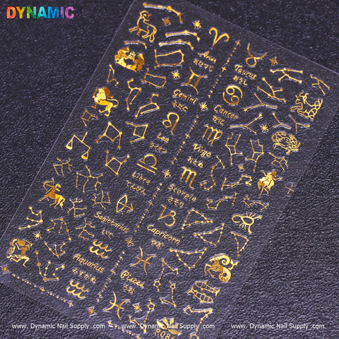 The Zodiac, Horoscope Nail Design Sticker - Gold from Dynamic Nail Supply showcases gold zodiac symbols and constellations set against a dark background. The horoscope-inspired stickers are organized in rows featuring signs such as Leo, Virgo, and Capricorn, with the brand name Dynamic Nail Supply appearing along the bottom edge.