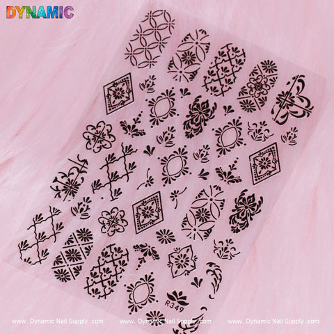 A sheet of Pattern Nail Sticker (R349) - Black from Dynamic Nail Supply features a black floral and geometric pattern on a soft pink background. Each row showcases intricate designs such as flowers, leaves, and diamonds. The top left corner displays the word "DYNAMIC" in colorful letters, adding a vibrant touch to this elegant set.