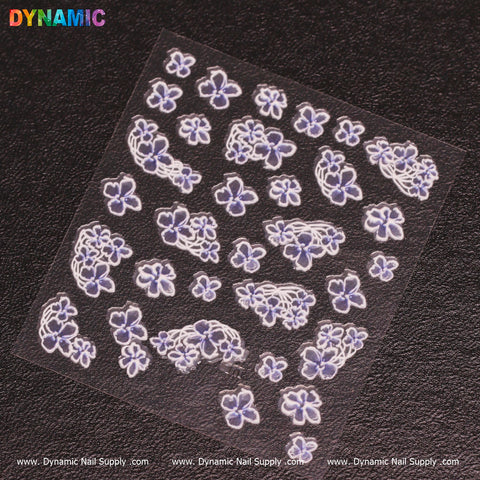 A sheet of small, intricately designed purple and white floral stickers set against a black background. This exquisite "Flower Sticker (10)" pack from Dynamic Nail Supply features flowers in diverse sizes with multiple petals, complemented by the brand name displayed in vibrant letters at the top.