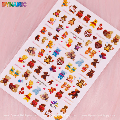 A sheet of vibrant teddy bear-themed nail decals on a pink background showcases the Cute Teddy Bear Sticker (R024), featuring adorable bears holding hearts, balloons, and gifts with phrases such as "The power of choice" and "I love you." The brand name, Dynamic Nail Supply, is prominently displayed at both the top and bottom edges.