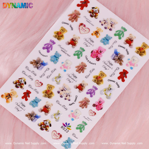 A sheet of Cute Teddy Bear Stickers (R022) featuring various designs such as bears in different poses, hearts, and phrases like Classic Teddy and Peace & Blanket. The adorable sticker set is displayed on a soft pink background with Dynamic Nail Supply branding along the bottom edge.