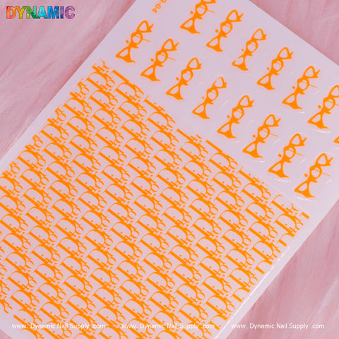 A sheet of neon orange luxury water decals from Dynamic Nail Supply is set against a pink background. These nail stickers showcase stylized cat faces with prominent whiskers arranged in neat rows. The top left corner features the word "DYNAMIC" in multicolored letters, while the bottom showcases the website: www.DynamicNailSupply.com.
