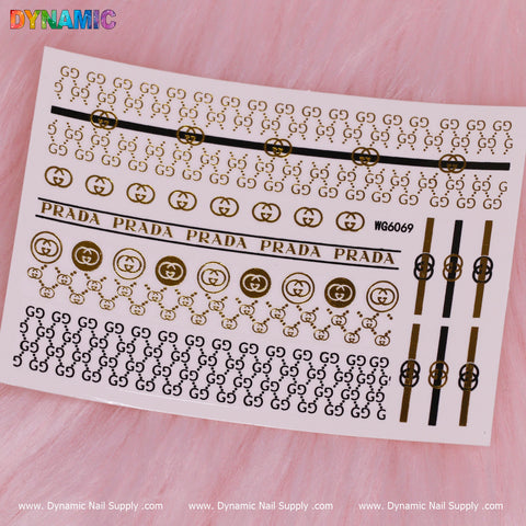 A sheet of Luxury Style Water Decal (WG6069) from Dynamic Nail Supply is set against a pink fur backdrop, displaying gold and black designs inspired by high-end brand logos. With interlocking letters and repetitive brand names, the bottom features multiple instances of "Dynamic Nail Supply," providing a stylish accent for nail enthusiasts.