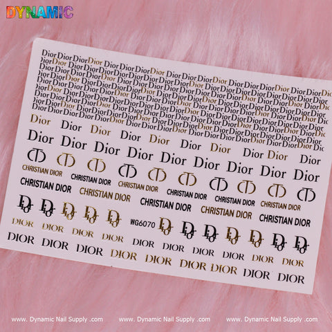 A water decal sheet labeled Luxury Style Water Decal (WG6070) from Dynamic Nail Supply is placed on a pink, fluffy background. It features Dior-themed nail art stickers, displaying the Dior logo and name in an array of sizes and styles, including black, gold, and hollow designs. The colorful DYNAMIC logo is displayed prominently in the top left corner.