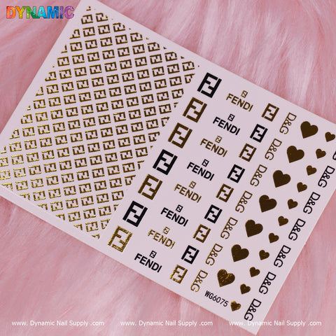 The Luxury Style Water Decal (WG6075) from Dynamic Nail Supply exudes opulence on a pink fur backdrop, featuring gold and black designs. The sheet showcases Fendi text, letter F logos, and symbols such as hearts and crowns in solid gold, black on white, and detailed lattice patterns for a sophisticated look.