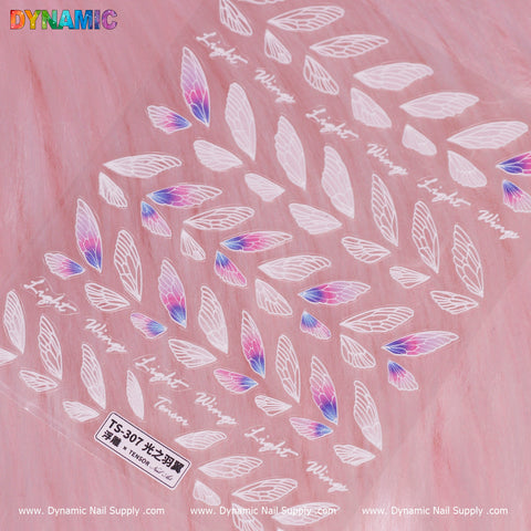 A card in pink showcases a pattern of various white and pink wing-shaped decals, some highlighted with purple and blue accents. "Light Wings" is prominently displayed, accompanied by additional text below and a TS-307 label. The rainbow-colored Dynamic Nail Supply logo embellishes the top left corner, making this Wings Sticker an eye-catching product.