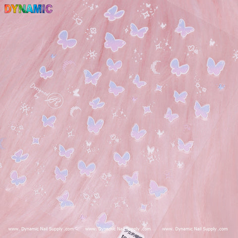 The "Dreamy Butterfly and Night Sticker" collection from Dynamic Nail Supply features a charming assortment of iridescent butterfly nail decals set against a soft pink backdrop. The butterflies come in various sizes and are accompanied by decorative stars and crescent moons, with the Dynamic Nail Supply branding elegantly placed along the top and bottom edges.