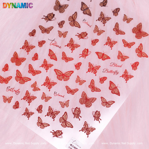 A sheet of Red Butterfly Stickers from Dynamic Nail Supply is showcased against a pink fur background. These stickers feature butterflies in various sizes with intricate details, alongside words like Blood Butterfly and Tatiana integrated into the design.