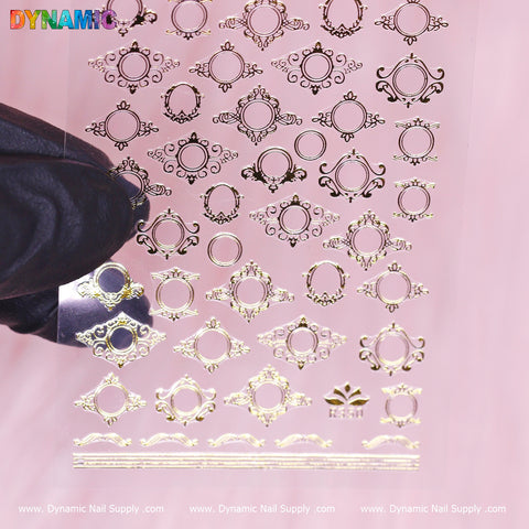 Close-up of a sheet of Dynamic Nail Supply's Mirror Style Sticker (R350) in gold metallic, held by a gloved hand. The mirror-style decals showcase ornate circular and floral designs against a pink background.