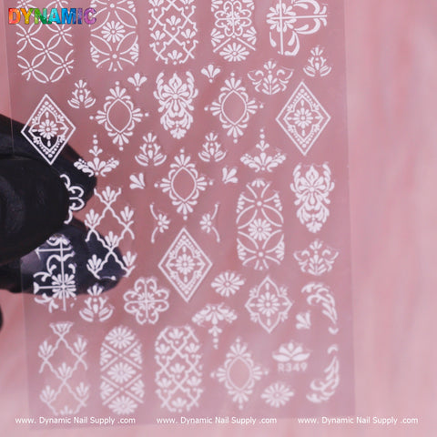 A close-up of the Pattern Nail Sticker (R349) - White reveals detailed floral and geometric designs. The stencil, held by a person wearing a black glove, exemplifies an elegant nail art accessory. The top features the brand name Dynamic Nail Supply, with www.DynamicNailSupply.com displayed at the bottom.