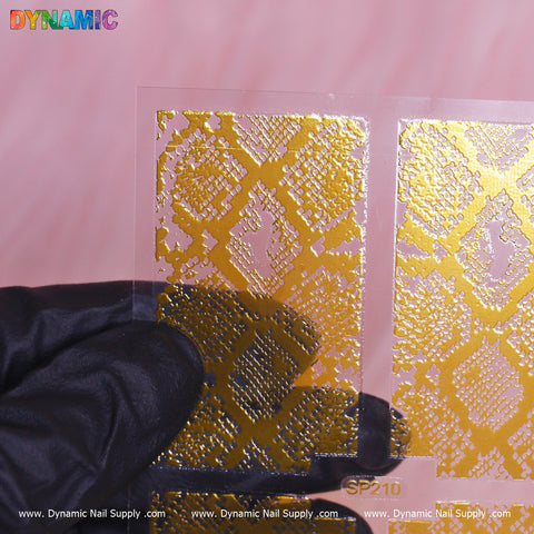 A gloved hand holds a transparent sheet from the Dynamic Nail Supply collection, featuring their intricate Animal Pattern Nail Sticker (SP210) with a snakeskin motif. The colorful DYNAMIC logo is prominently displayed in the top left corner, all set against a soft pink background.