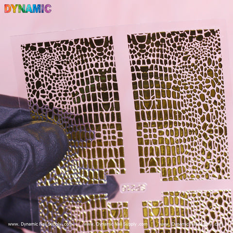 A gloved hand presents the Animal Pattern Nail Sticker (SP216) from Dynamic Nail Supply, featuring detailed animal design stencils. Set against a pink background, the word "DYNAMIC" appears in vibrant letters at the top left, while website details accompany this striking nail sticker close-up at the bottom.