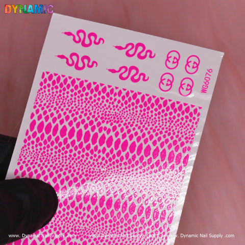 A close-up showcases a hand holding a neon pink nail decal sheet titled "Snake Skin Nail Water Decal (WG6076)" from Dynamic Nail Supply. The sheet features vibrant snake skin patterns and textured designs that resemble scales, with the brand's logos and website details visible on it, resting against a soft pink surface.
