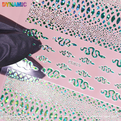 A gloved hand holds a pink stencil sheet with cut-out designs over a green holographic background, featuring wavy patterns reminiscent of snake skin. The word DYNAMIC is printed in multicolored text in the top left corner, with "Dynamic Nail Supply" and "Snake Skin Nail Water Decal (WG809) - Green Holographic" at the bottom edges.