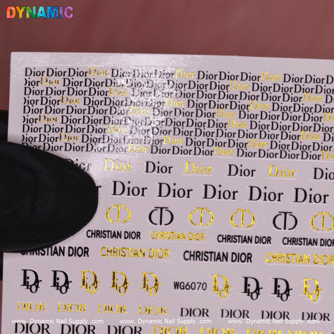 A close-up of the Luxury Style Water Decal (WG6070) from Dynamic Nail Supply showcases repetitive gold and black text designs that exude elegance. The text features the word Dior along with the brand's logo. "DYNAMIC" is prominently displayed in colorful letters at the top, while a black object partially obscures the left side of this sheet.