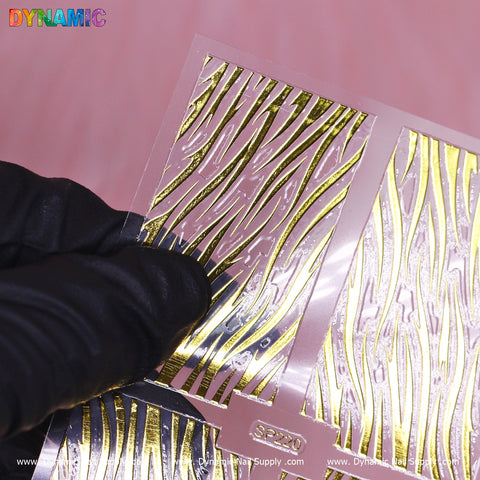 A hand wearing a black glove holds a sheet of Animal Pattern Nail Stickers (SP220) from Dynamic Nail Supply. The design showcases dynamic zebra-like stripes on a transparent backing. The left sticker is being peeled off, and the word DYNAMIC is visible in the top left corner of the image.