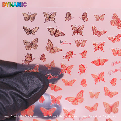 A gloved hand holds a clear plastic sheet featuring an array of vibrant butterfly designs and adorned with text like "Blood and Butterfly." The bottom prominently displays the brand name, Dynamic Nail Supply. The background is softly hued in pink, highlighting the Red Butterfly Sticker.