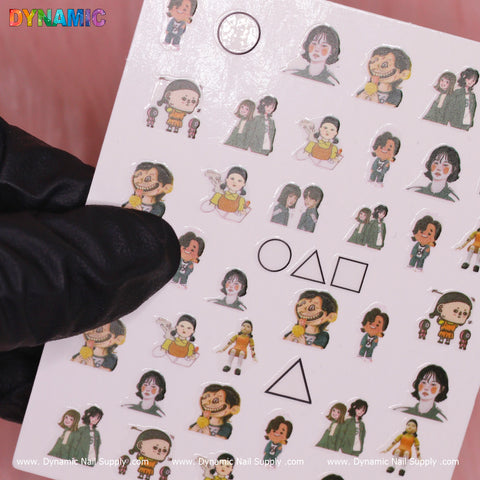 A set of nail stickers from Dynamic Nail Supply's "Squid game 03 (sq game)" collection features cartoon characters and geometric shapes such as circles, triangles, and squares. Some characters are dressed in outfits reminiscent of "Squid Game," offering a playful twist. The sheet is held against a pink background by a black-gloved hand.