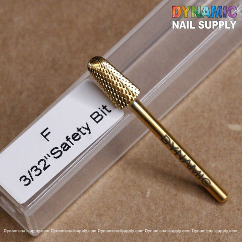 A close-up of a gold F Safety Bit - Dynamic Drill Bit, marked as 3/32 Safety Bit on the packaging. The brand name, Dynamic Nail Supply, is embossed on the bit. Colorful text displaying "Dynamic Nail Supply" appears in the top right corner. The bit is placed on a clear plastic case.
