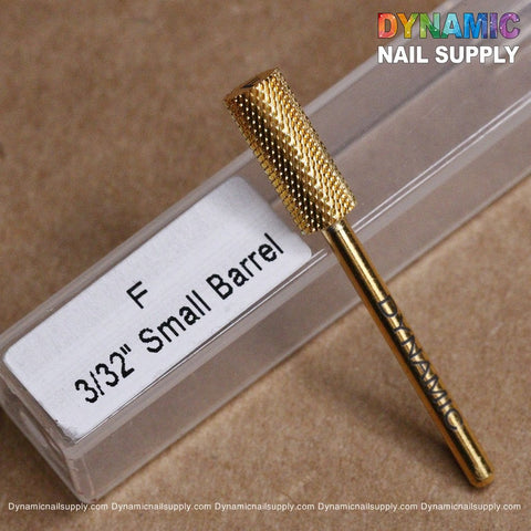 A gold-toned tungsten carbide nail drill bit with a textured surface, bearing the "DYNAMIC" label, rests beside its packaging. The packaging is marked with "Small Barrel - Easy And Safe To Use for Smooth-out Acrylic (F 3/32)." The background is a light brown surface, and the logo text at the top right says "Dynamic Nail Supply.