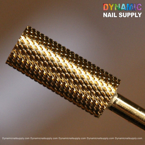 The image showcases a close-up of the Fine (F) Small Barrel tungsten carbide nail drill bit from Dynamic Nail Supply, featuring a gold-colored cylindrical shape with a textured surface. The softly blurred background emphasizes the drill bit's design. The top right corner displays the colorful Dynamic Nail Supply logo, and the text "Dynamicnailsupply.com" is repeated at the bottom for emphasis.