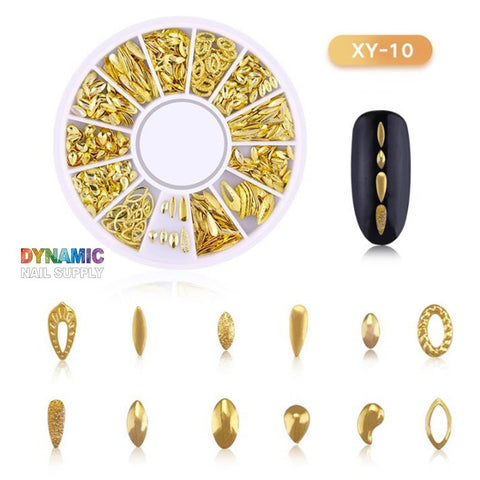 A display featuring the Gold Metal Frame for Nail Art Designs - Part 2 by Dynamic Nail Supply showcases a variety of nail designs with gold metallic teardrop, oval, and leaf-shaped decorations. Adjacent to it, a black nail adorned with three gold accents sparkles, accompanied by the text XY-10 and Dynamic Nail Supply, providing inspiration for creative nail art.