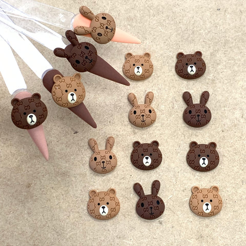 These clay hair clips feature the Logo pattern Brown & Cony charms for nail art design by Dynamic Nail Supply, making them perfect for capturing attention on Instagram. Arranged on a light brown surface, the cartoon-like animal head designs atop cone bases create a delightfully whimsical effect in shades of brown.