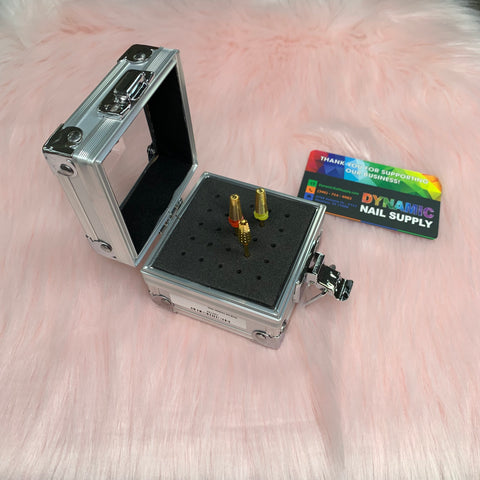 A stylish aluminum Drill Bit Holder by Dynamic Nail Supply, featuring a black foam insert for three drill bits, is elegantly placed on a soft pink, fluffy surface next to a vibrant business card showcasing "Dynamic Nail Supply.