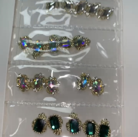 A close-up of a jewelry display highlights four rows of rings, each adorned with the iridescent stones that resemble Dynamic Nail Supply's Pre-made Nail Charms. The decorative bands feature multiple vibrant gems reflecting brilliant colors under the light, much like the charms designed for nails. These rings are organized neatly in a transparent plastic case.