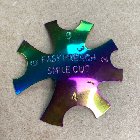 A rainbow-colored metallic nail tool from Dynamic Nail Supply, known as the French Nails Cutter - Acrylic Trimer to create French Nails easier, features six numbered notches around the phrase EASY FRENCH SMILE CUT. These notches, labeled 1 to 6 and evenly spaced, are set against a textured brown background.