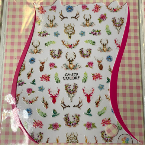 The CA-270 COLORF sheet from Dynamic Nail Supply's Bundle of 20pcs Christmas Nail Stickers for $30 presents a decorative array of multicolored designs on a white background, including antlers, floral arrangements, deer heads, and skulls. It is framed by a pink border against a pink and white checkered surface.