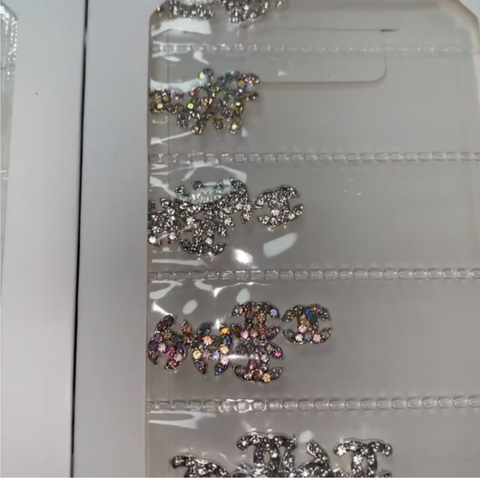 Dynamic Nail Supply's Pre-made Nail Charms are vibrant, multicolored rhinestone gems for nails, designed in various shapes and showcased on a clear tray with convenient slots for easy organization. These shimmering charms capture the light beautifully, providing a dazzling effect ideal for any nail designer.