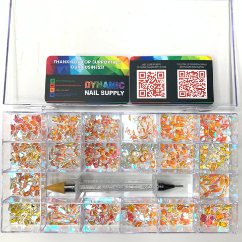 A nail art kit contains a clear, divided plastic box filled with blue aurora and iridescent rhinestones. Two business cards featuring QR codes and the vibrant branding of Dynamic Nail Supply are displayed above, accompanied by a message of appreciation. A dual-ended crystal gem tool is placed on top of the box.