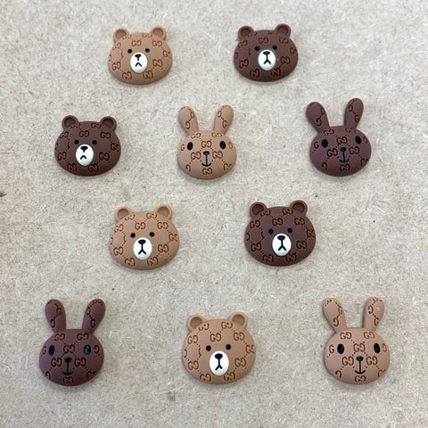 Enhance your next Instagram post with the Logo pattern Brown & Cony charms for nail art design by Dynamic Nail Supply. These ten animal face charms feature five bear and five rabbit faces in light and dark brown shades, complete with GG logo patterns. Arrange them in a stylish layout with bears on the top and middle rows, while rabbits fill the second and bottom rows, creating a textured and charming surface.