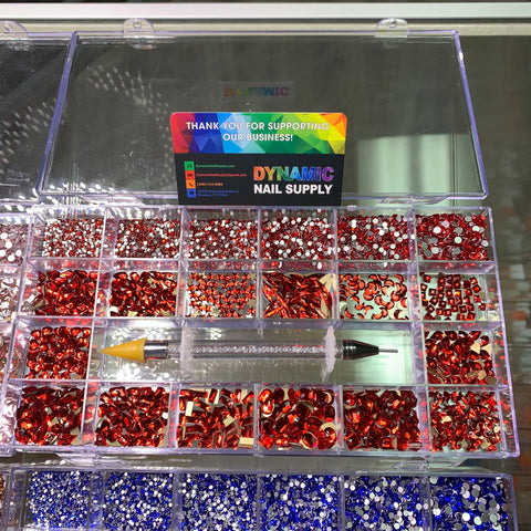 A clear plastic organizer holds Bling Bling sets of red and silver nail decorations, featuring rhinestones, sequins, and small glittery shapes. At the center, a rhinestone picker with a barrel filled with glitter is included. A colorful card on top says "Thank you for supporting our business - Dynamic Nail Supply.