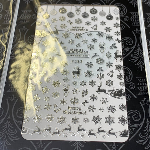 A silver stamping plate features intricate Christmas-themed designs such as snowflakes, ornaments, reindeer, and a sleigh with gifts. For the perfect festive manicure, pair it with Dynamic Nail Supply's Bundle of 20pcs Christmas Nail Stickers for $30. The reflective surface creates subtle light patterns on the black background.