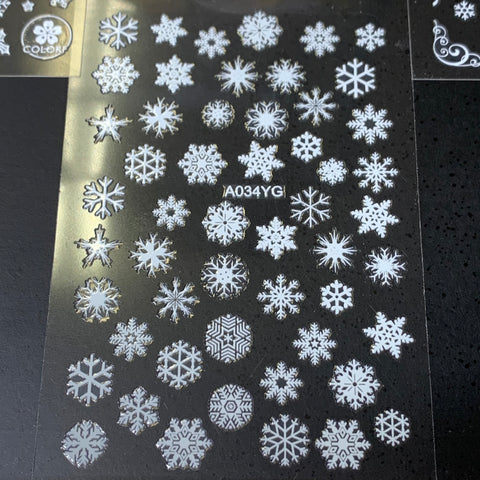 A sheet in black hosts an array of 20 intricate and unique white snowflake designs, ideally suited as Christmas nail stickers. Each piece is evenly arranged around the center code A034YG, with a decorative border located in the top right corner. This $30 bundle is offered by Dynamic Nail Supply.