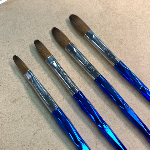 Four Dynamic Kolinsky Brushes with blue, metallic handles are laid side by side on a brown surface. Ideal for acrylic application, these brushes from Dynamic Nail Supply feature round, brown bristles and are labeled in sizes #2 to #8. Their faceted design reflects light beautifully.