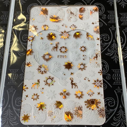 A set of 20 Christmas nail stickers for $30 by Dynamic Nail Supply showcases festive metallic gold snowflakes, reindeer, and various holiday motifs on a white background, labeled F719 and presented on a wavy patterned black backdrop.