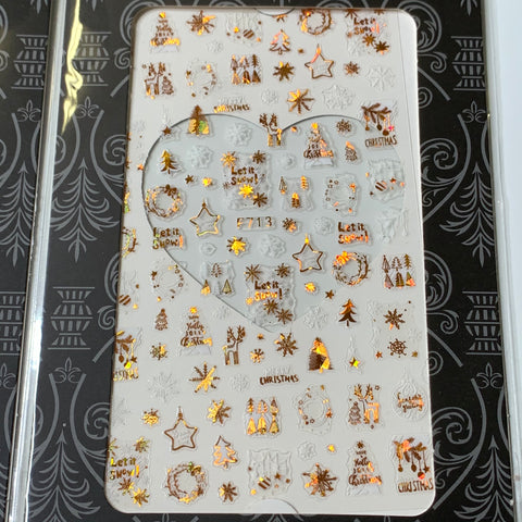 Introducing the Dynamic Nail Supply's Bundle of 20pcs Christmas Nail Stickers for $30. This festive collection features metallic orange and gold snowflakes, Christmas trees, wreaths, and stars. The stickers are elegantly set against a white background with black borders and include phrases like "Let it Snow" to enhance the holiday spirit.