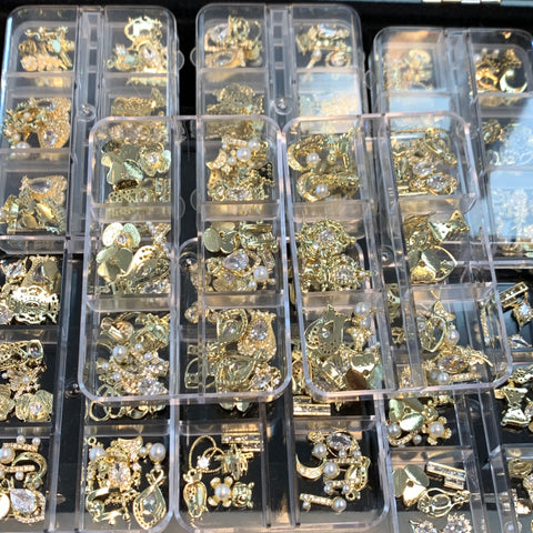 The 30-piece set of nail charms from Dynamic Nail Supply, featuring random shapes and intricate patterns, includes a variety of gold and silver jewelry findings such as pendants and crystals. These items are designed for nail art decoration and are organized in clear plastic compartments, with glimmering details and pearl accents that catch the light beautifully.
