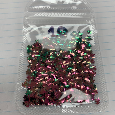 A small, transparent bag containing Dynamic Nail Supply's Maple Leaves Sequin for Nails Art Design is filled with color-shifting fall leaf glitter in the shapes of maple leaves. The confetti features hues like green, pink, and gold. This fall leaf sequin bag is sealed and set against a lined notebook paper backdrop with the number 10 written in blue ink at the top.