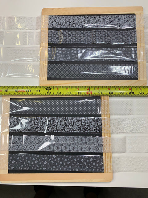 Two wooden-framed trays are adorned with sheets of patterned black and white paper. A yellow measuring tape runs across the center, displaying measurements in inches. Surrounding the trays are transparent, textured plastic sheets from Dynamic Nail Supply's Designer Foils collection (style #001), known as New Designer Foils – 8 rolls, each 2ft long.