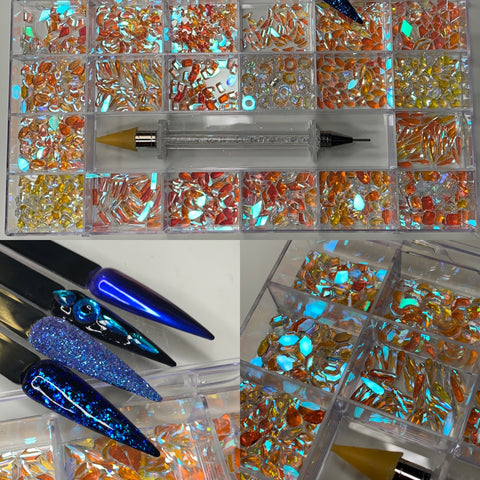 The Dynamic Nail Supply display features an assortment of 1000 pcs of Iridescent Blue Aurora Clear Crystal Rhinestones in various shapes, arranged neatly. Below the rhinestones, three blue stiletto-shaped nails are artfully adorned with these vibrant crystals and shimmering glitter. A gem applicator tool is also included among the nail art supplies for precise application.