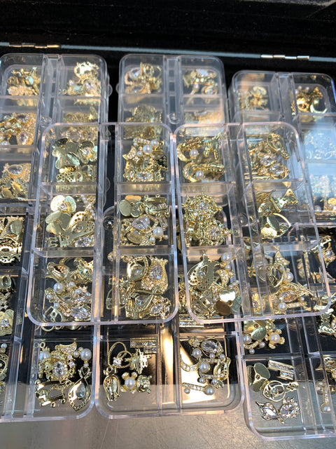 The Dynamic Nail Supply offers a set of 30 gold-colored nail charms for nail art design and decoration, featuring an assortment of random shapes. Each charm may be embellished with pearls or crystals, neatly organized in clear plastic compartments to showcase a rich variety of intricate designs.