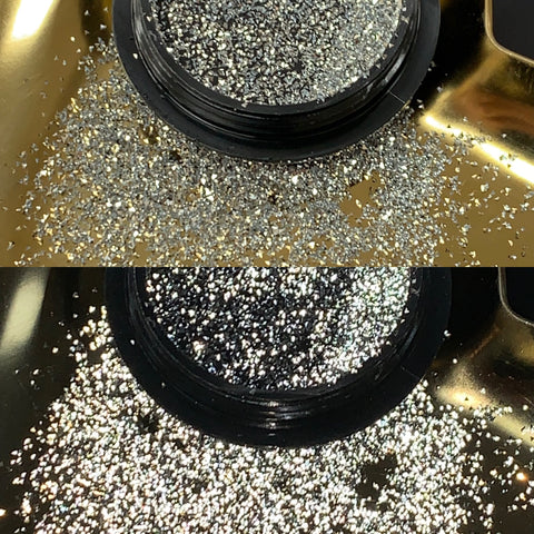 A close-up captures the lid of a Reflective Pixie container by Dynamic Nail Supply, set against a gold surface. Fine silver glitter spills from the black container, with the upper part showing a concentrated cluster and the lower part spreading out elegantly like nail art magic. This creates an enchanting sparkle effect against the shimmering gold backdrop.